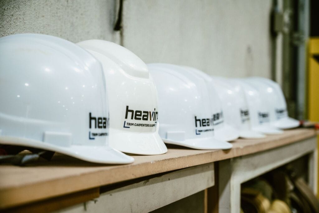 Row of white Heavin Trim Carpenters & Supply hard hats lined up on a workbench