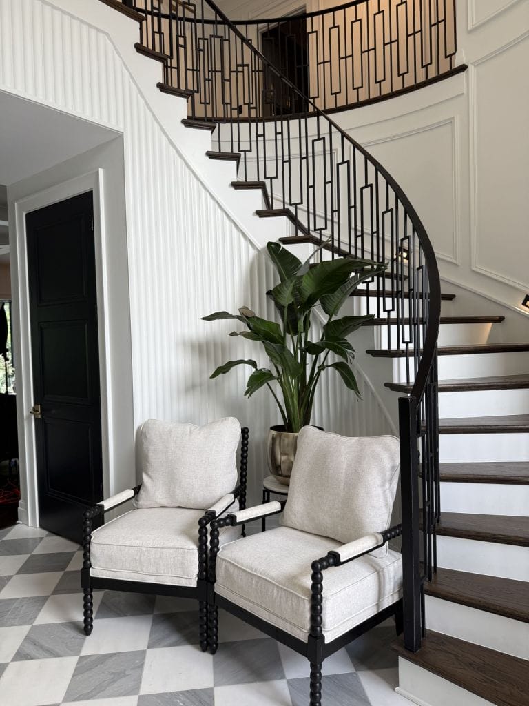 Curved staircase with black metal railing beside a white shiplap wall and dark interior door