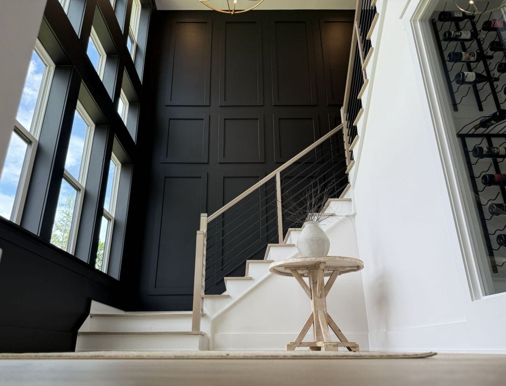 Dark paneled stairwell wall with picture-frame moulding and a modern cable-rail staircase